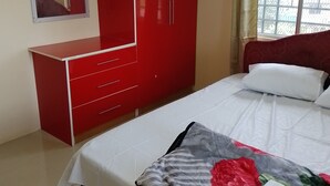 Un dormitorio con cama, un armario rojo, un espejo y una ventana con cortinas.
