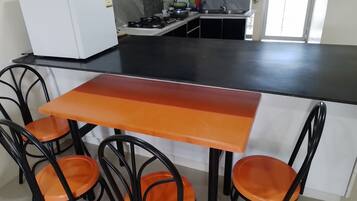 Et kompakt køkken med en sort bordplade, hvide skabe og en lille vask. Fire orange stole står ved et bord.