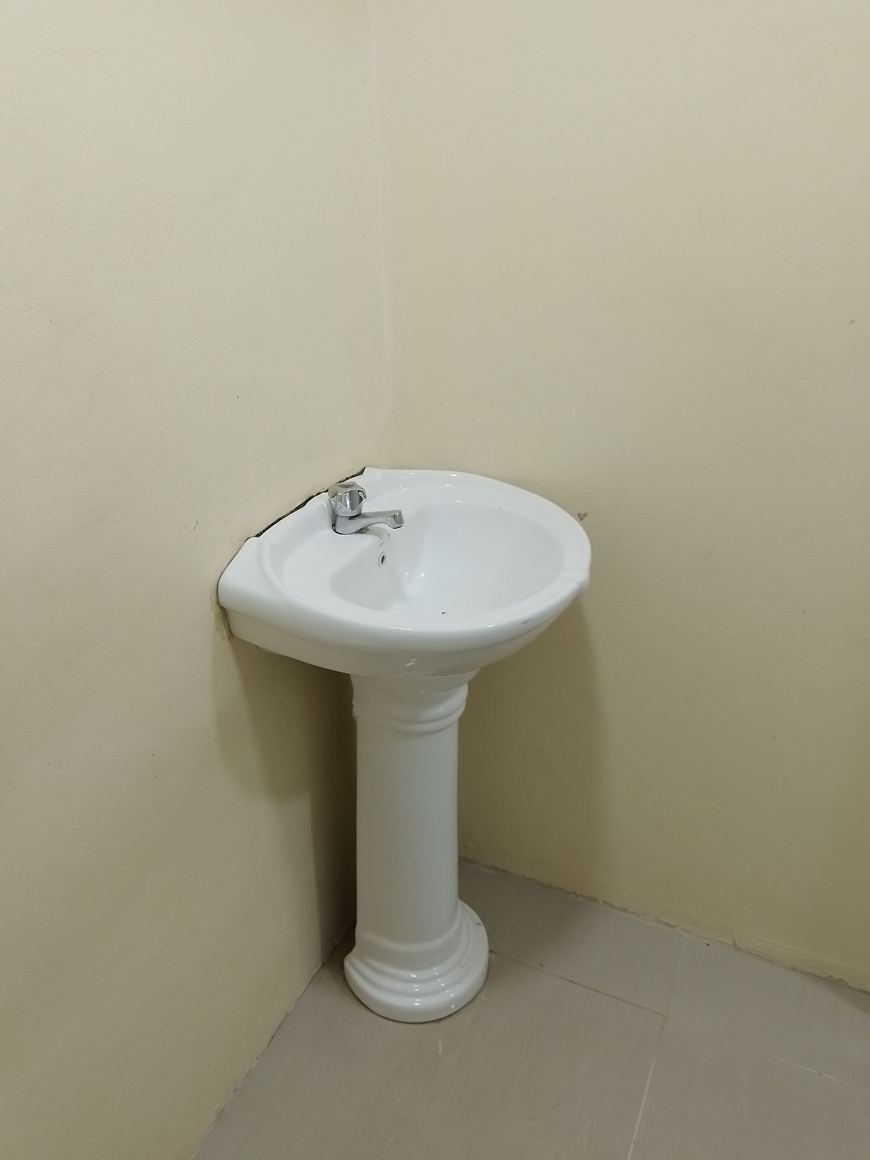 Ein weißes Waschtuch mit einem einzelnen Wasserhahn, an einer beigen Wand in einer Ecke angebracht.