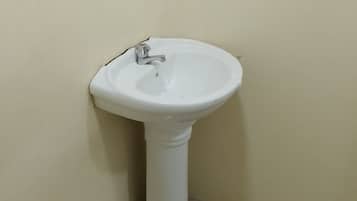 Ein weißes Waschtuch mit einem einzelnen Wasserhahn, an einer beigen Wand in einer Ecke angebracht.