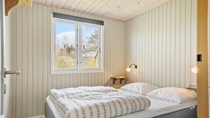 Un dormitorio con cama, ventana y mesita de noche con lámpara.