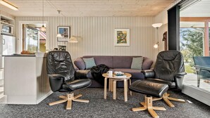 Una sala moderna con un sofá, dos sillones de cuero, una mesa de centro y una cocina con refrigerador y microondas.