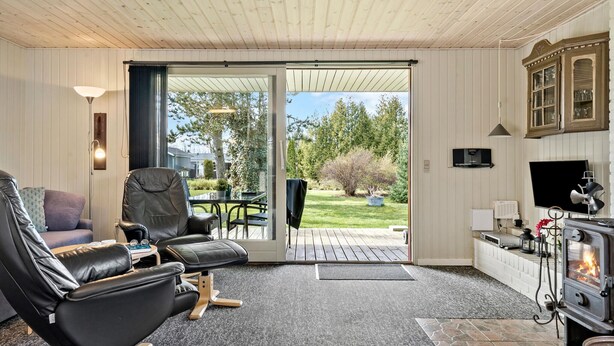 Un salón acogedor con chimenea, sillones de cuero, televisor y puerta corrediza de cristal que da a un jardín.