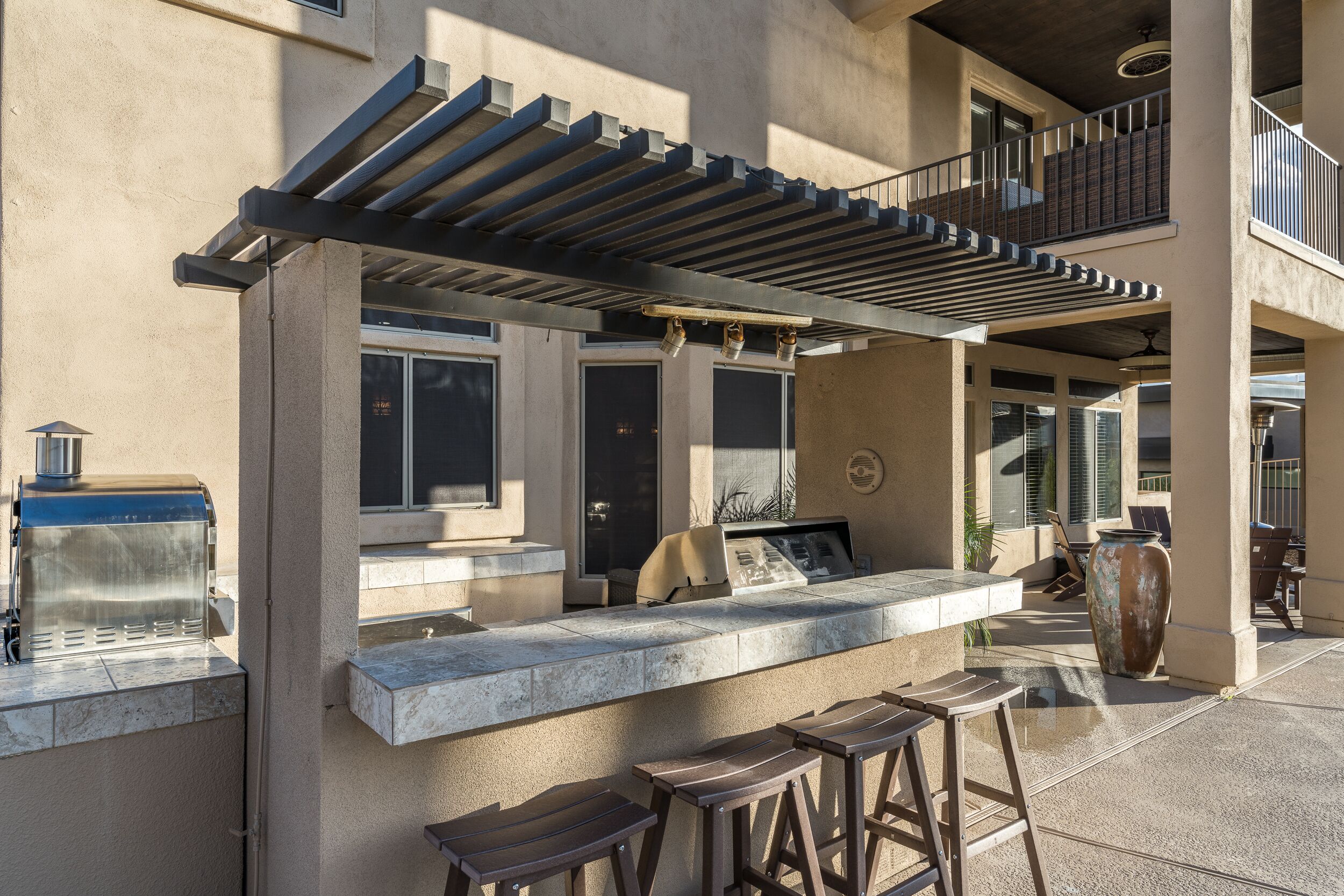 An outdoor bar area with a pergola, seating, and a grill.
