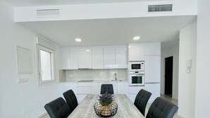 A modern kitchen with white cabinets, a built-in oven, and a dining area with a marble table and black chairs. - Villa Tranquilidad (Avileses) (Avileses)