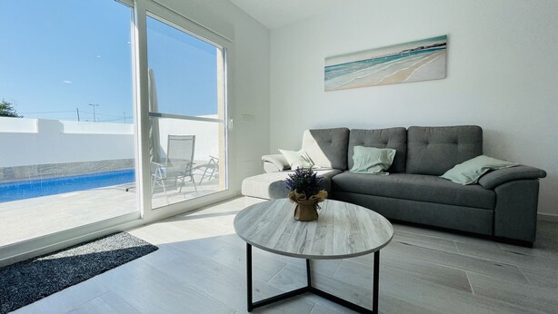 A modern living room with a grey sofa, a round coffee table, and a painting of a beach scene. - Villa Tranquilidad (Avileses) (Avileses)