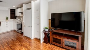 Eine moderne Küche mit weißen Schränken, einem eingebauten Backofen und einem großen Flachbildfernseher auf einem Holzboden.