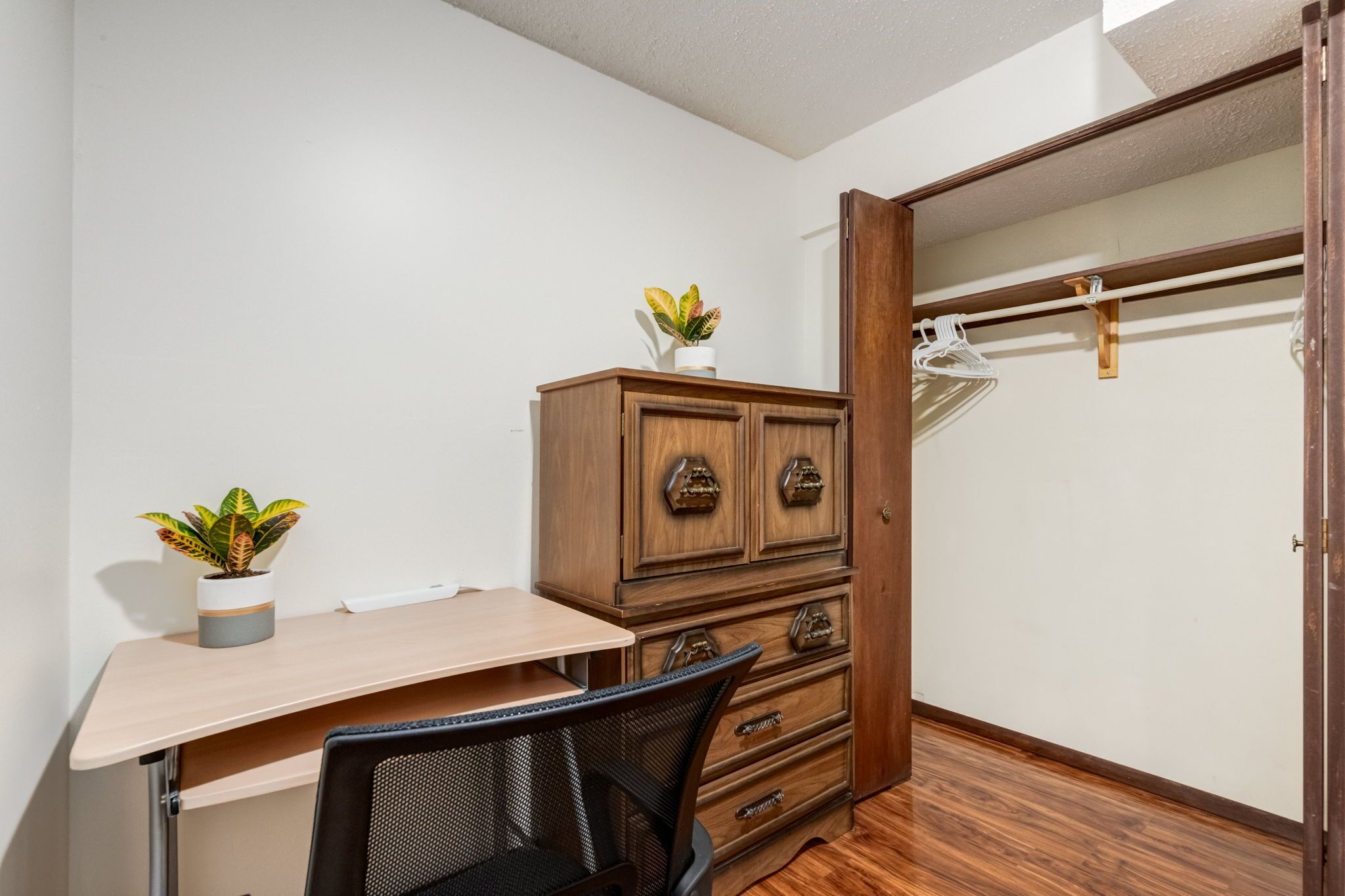 A small room with a desk, chair, wooden dresser, and a walk-in closet.