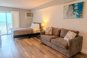Un dormitorio con cama, sofá, mesita de noche, lámpara y un cuadro en la pared.