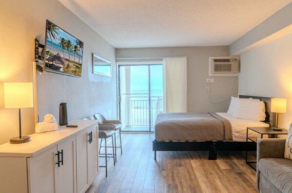 A hotel room with a bed, a desk, a chair, a balcony, and an air conditioning unit.