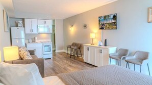 A compact hotel room with a bed, a desk, a kitchenette, and a seating area with chairs. - Sea Mist 20407 (Myrtle Beach)