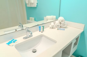 A bathroom with a white sink, a mirror, and toiletries including towels and personal care products.