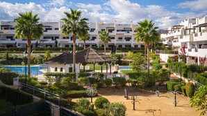 Un complex turístic amb diversos edificis blancs, palmeres, una piscina i una glaçada.