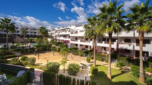 Un complex turístic amb diversos edificis blancs, palmeres i un pati ben cuidat amb equipament esportiu.
