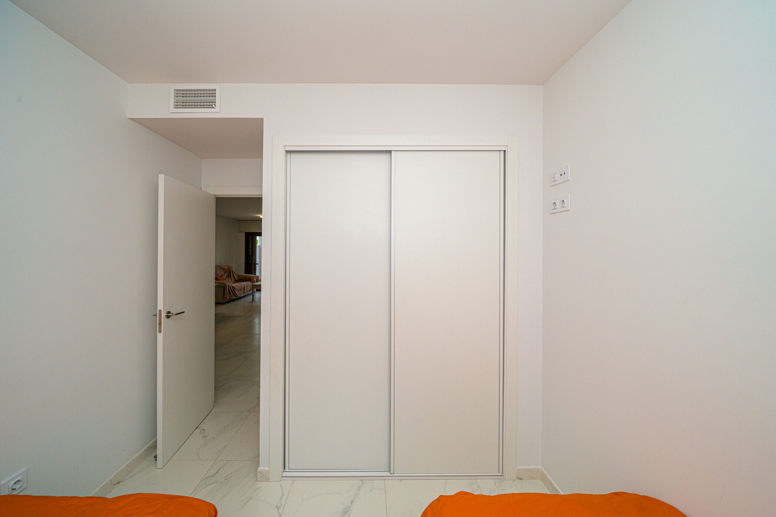 Una habitación con un armario cerrado, una puerta que da a otra estancia y un enchufe en la pared.