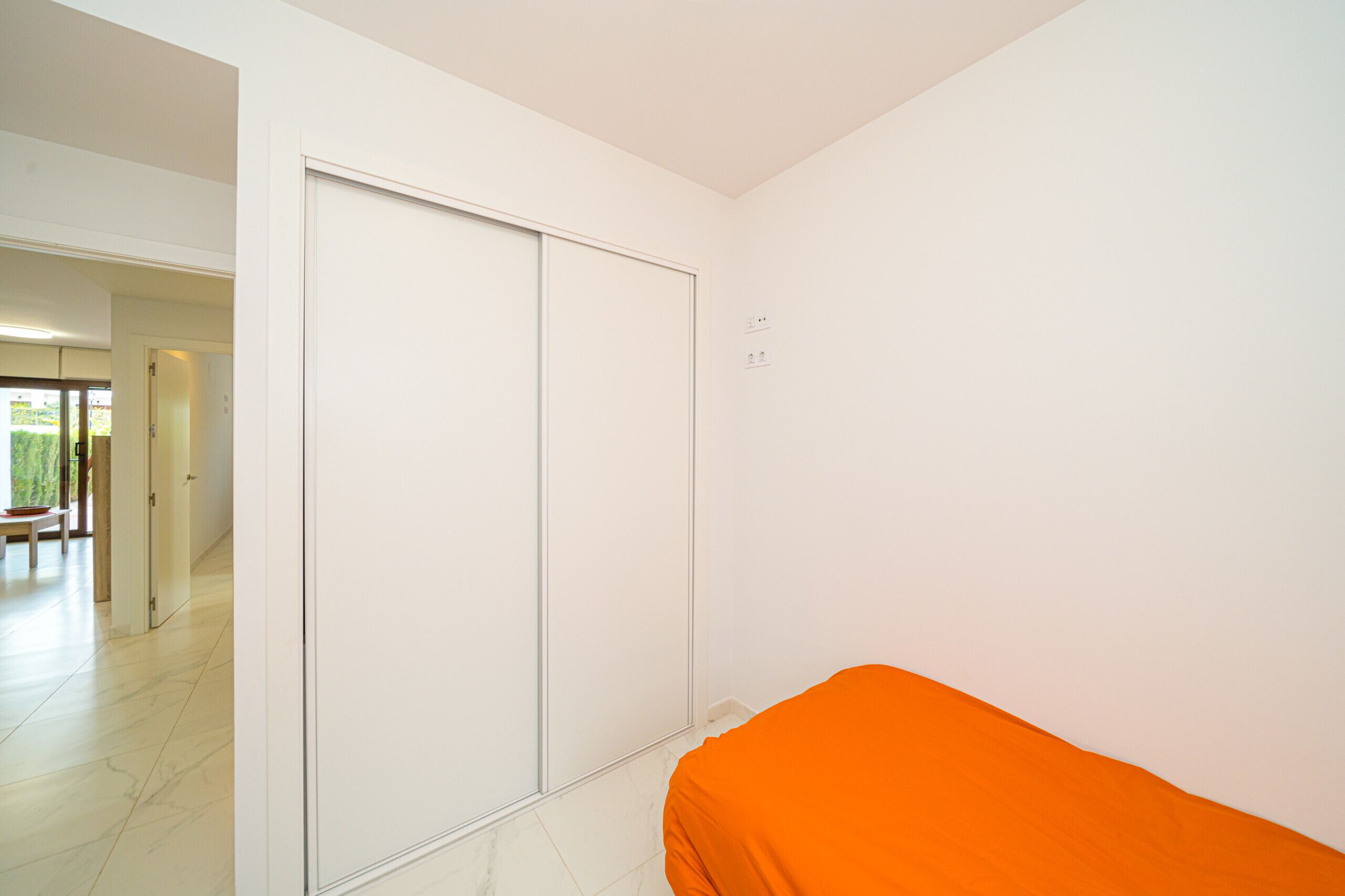 A room with a sliding door, a bed with an orange cover, and a tiled floor.