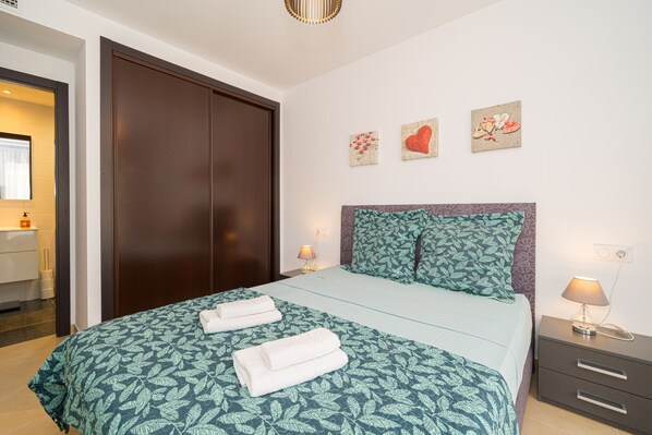 A hotel room with a bed, a nightstand, a lamp, and a wall with three decorative items.