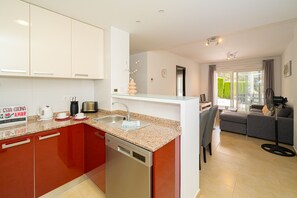 A modern kitchen with a dishwasher, a coffee maker, and a toaster. There is a dining area with a sofa and a fan. - Apartamento Mariphils (Linnea Sol) (Orihuela Costa)