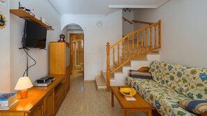Ein Wohnzimmer mit einer Couch, einem Fernseher, einer Holzkommode und einer Treppe.