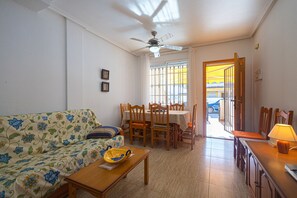 A living room with a sofa, dining table, chairs, and a ceiling fan.