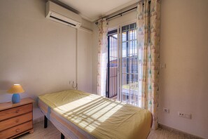 Een slaapkamer met een bed, een dressoir, een airconditioning en een raam met gordijnen met een patroon.