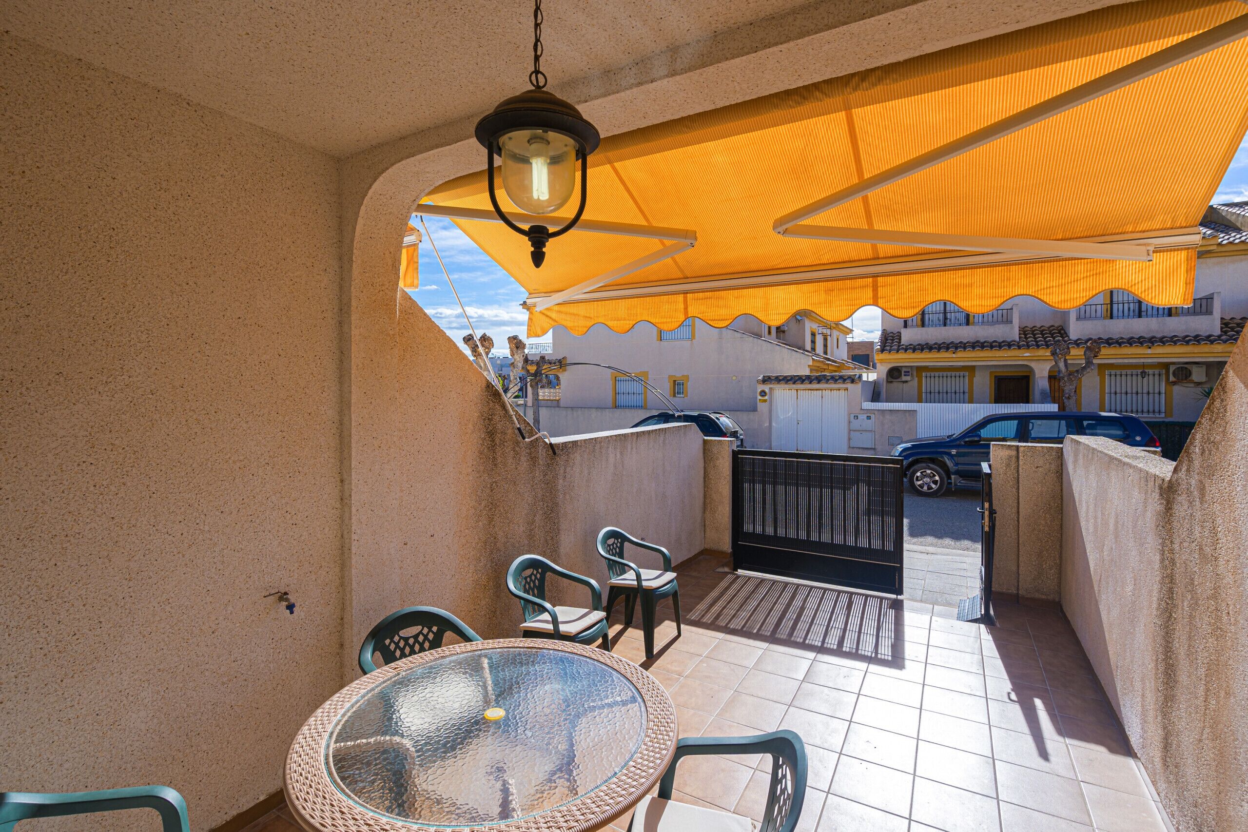 Un balcon avec une table et des chaises en verre, un luminaire suspendu et un auvent jaune.
