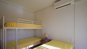Une chambre avec un lit superposé, un lit simple et une table de chevet avec une lampe.