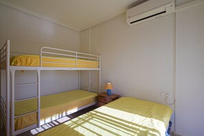 Une chambre avec un lit superposé, un lit simple et une table de chevet avec une lampe.