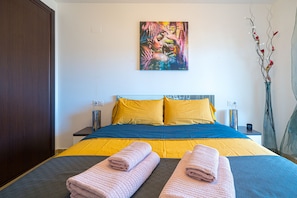 Une chambre d’hôtel avec un lit, des oreillers, un tableau, un vase avec des branches et une table de chevet avec une lampe.