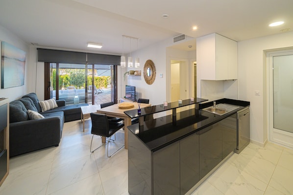 A modern kitchen with a central island, a dining area with a sofa and chairs, and a view through the glass doors.