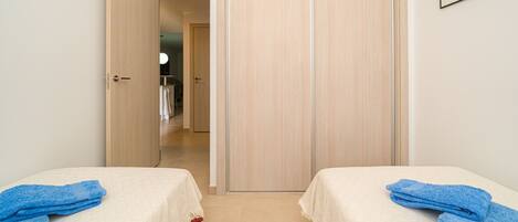 A hotel room with two beds, each with a blue towel and a white bedspread. There is a wooden wardrobe and a framed picture on the wall.