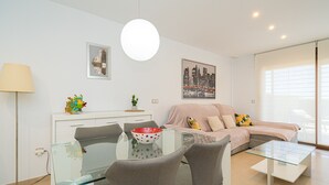A modern living room with a glass dining table, grey chairs, a sofa with cushions, a cityscape painting, and a floor lamp. - Apartamento Fleur et Soleil (Orihuela Costa)