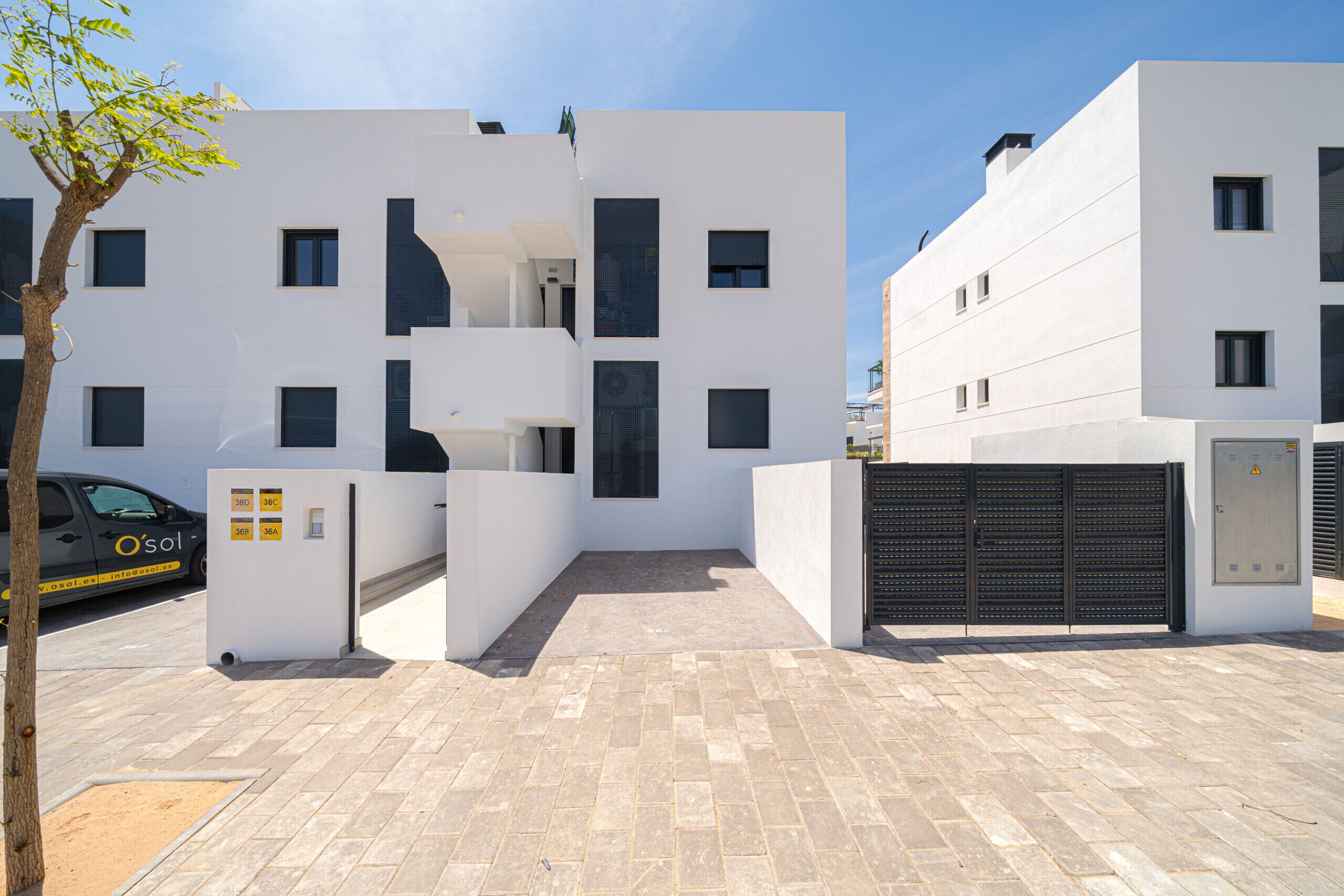 Un bâtiment moderne à la façade plate, doté de nombreuses fenêtres et d’une entrée fermée par un portail.
