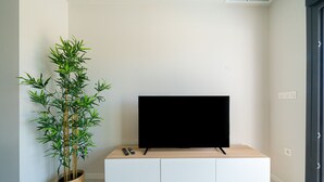 A modern living room with a flat-screen TV on a wooden console, a bamboo plant in a woven basket, and a door to the right. - Apartamento Iseo (Mil Palmeras) (Pilar de la Horadada)