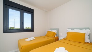 A room with two beds, each with a white headboard and yellow bedding. There is a window with a view of trees and a street lamp outside. - Apartamento Iseo (Mil Palmeras) (Pilar de la Horadada)