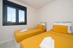 Een kamer met twee bedden, elk met een wit hoofdeinde en gele beddengoed. Er is een raam met uitzicht op bomen en een lantaarnpaal buiten.