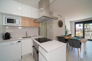 Une cuisine moderne avec des meubles blancs, un four à micro-ondes encastré, une machine à café et un coin repas comprenant une table et des chaises.