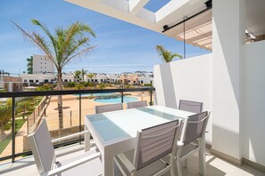 Een balkon met een glazen tafel en stoelen, met uitzicht op een zwembad en palmbomen.