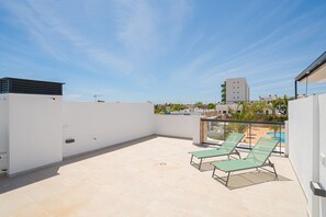 Une terrasse sur le toit, avec deux fauteuils de jardin, une vue dégagée sur les bâtiments environnants et une piscine en arrière-plan.