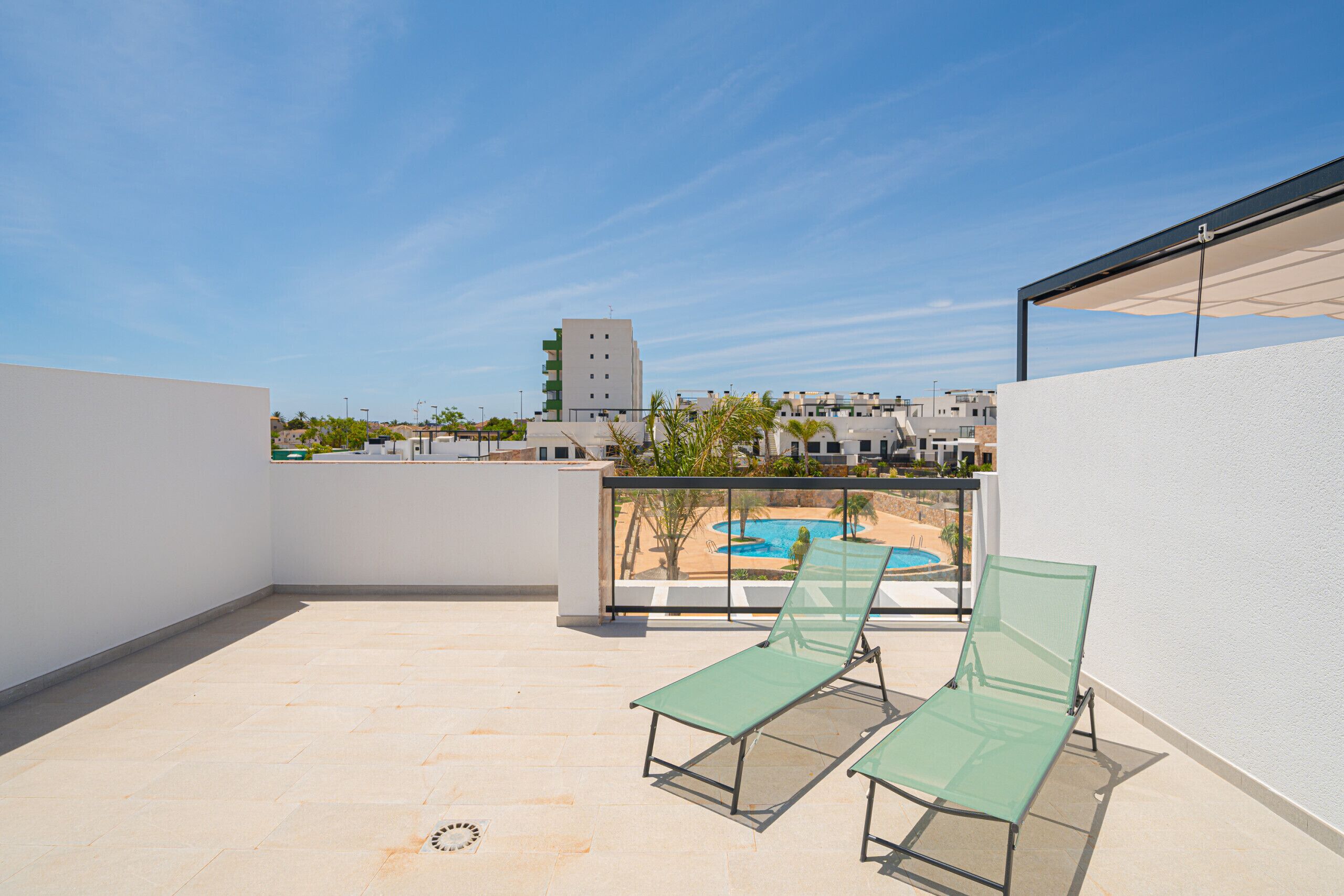 A rooftop terrace with two green lounge chairs, a pool, and a clear view of the surrounding buildings.