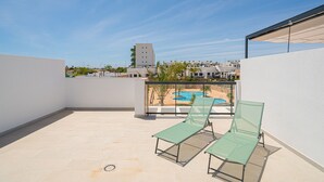 A rooftop terrace with two green lounge chairs, a pool, and a view of buildings in the background. - Apartamento Iseo (Mil Palmeras) (Pilar de la Horadada)