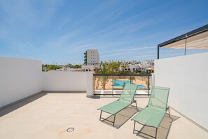 A rooftop terrace with two green lounge chairs, a pool, and a view of buildings in the background.