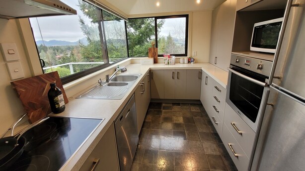 Een moderne keuken met een groot raam, roestvrijstalen apparatuur en uitzicht op de omgeving.