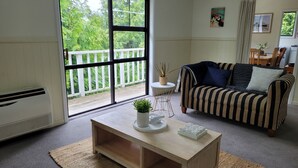 Een woonkamer met een groot raam, een gestreepte bank, een klein rond tafeltje en een houten salontafel met een plant.