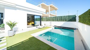 A modern house with a swimming pool, a covered outdoor area, and a view of a forested area.