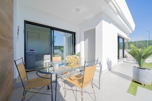 A modern outdoor dining area with a glass table and wicker chairs, a potted plant, and a view of the surrounding landscape.