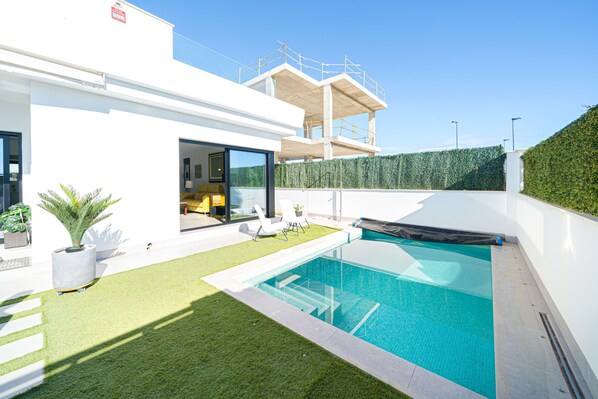 A modern house with a swimming pool, a covered patio, and a view of the construction site.