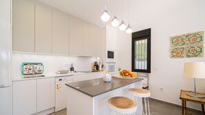 A modern kitchen with white cabinets, a central island with stools, a microwave, and a fruit bowl.