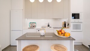 A modern kitchen with a central island, white cabinetry, a microwave, an oven, and a fruit bowl.