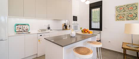 Una cocina moderna con una isla central, taburetes de bar, microondas y un frutero.